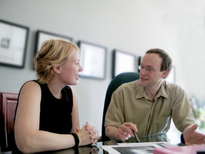 Two professionals, one man in glasses and one women, in a discussion at a table